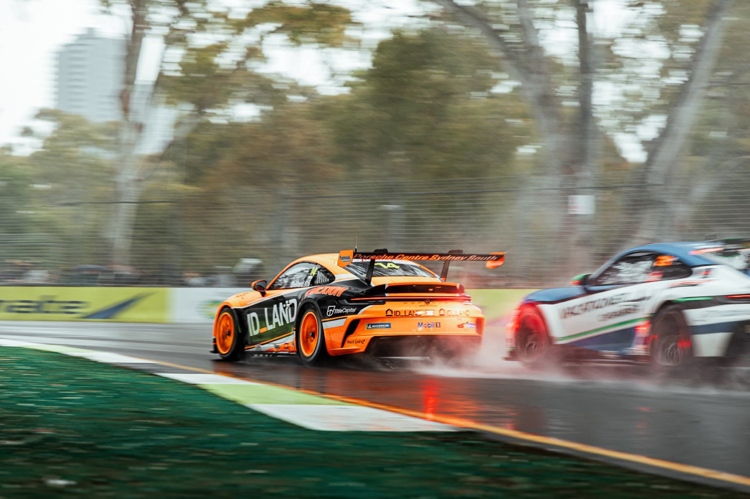 Two Porsche race cars throwing up spray on a wet track