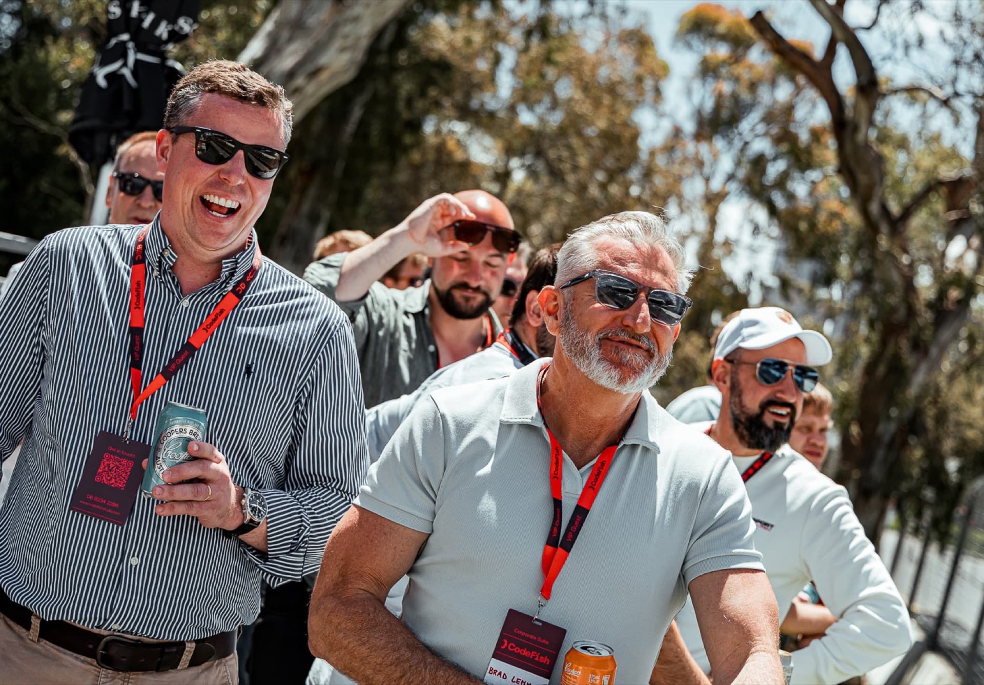 A group of guests in sunglasses and red lanyards laughing together at the track