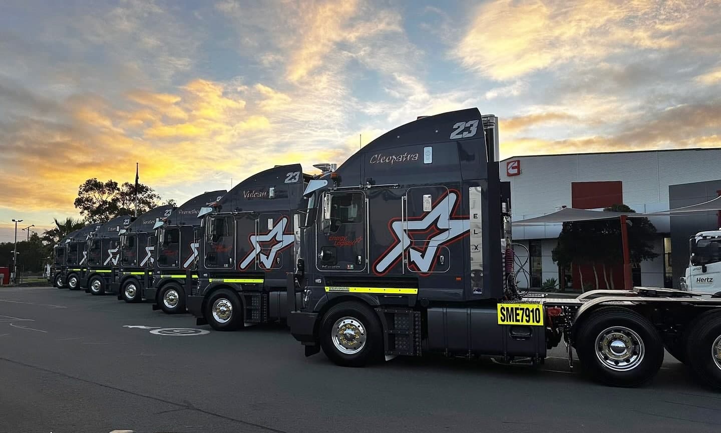 A row of dark prime movers parked outside a depot at sunset