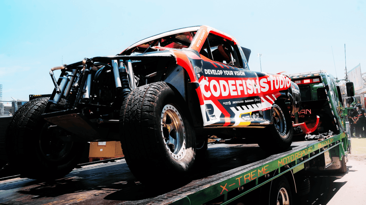 CodeFish Studio race truck loaded onto a motorsport transporter flatbed in the pits
