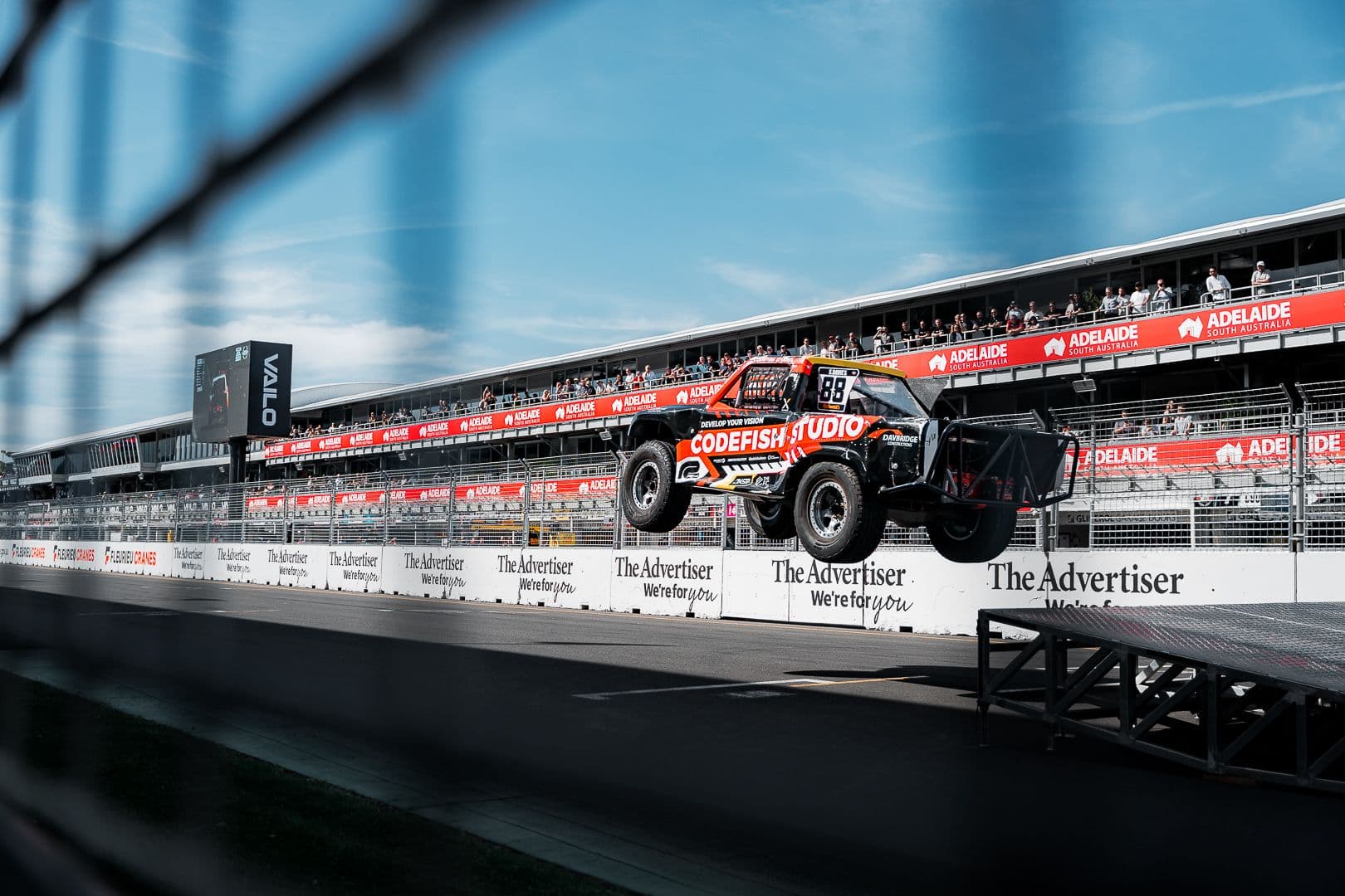 CodeFish Studio race truck landing a jump on the main straight in front of grandstands