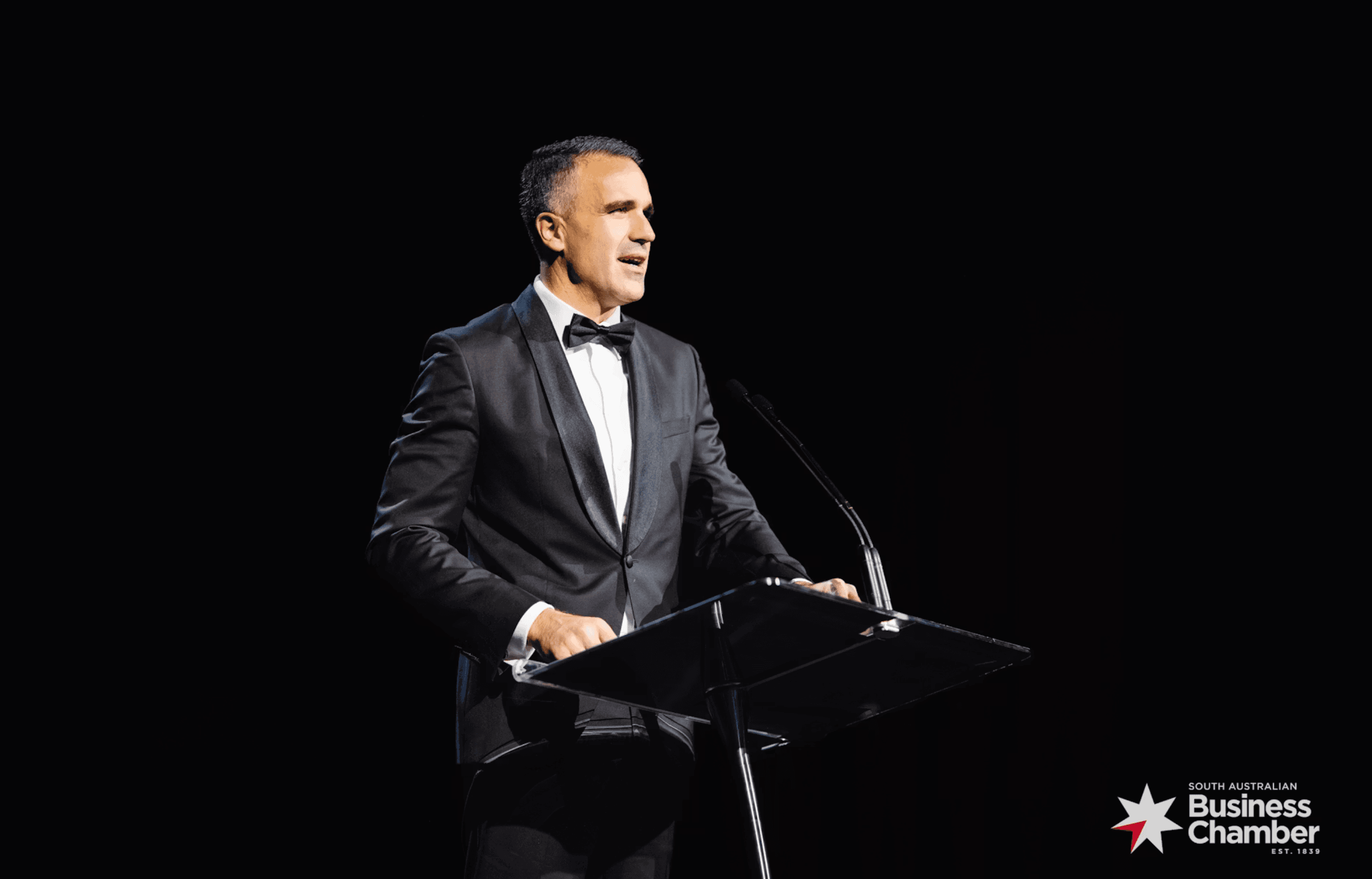 A speaker in black tie addressing the Business and Export Awards audience from a lectern