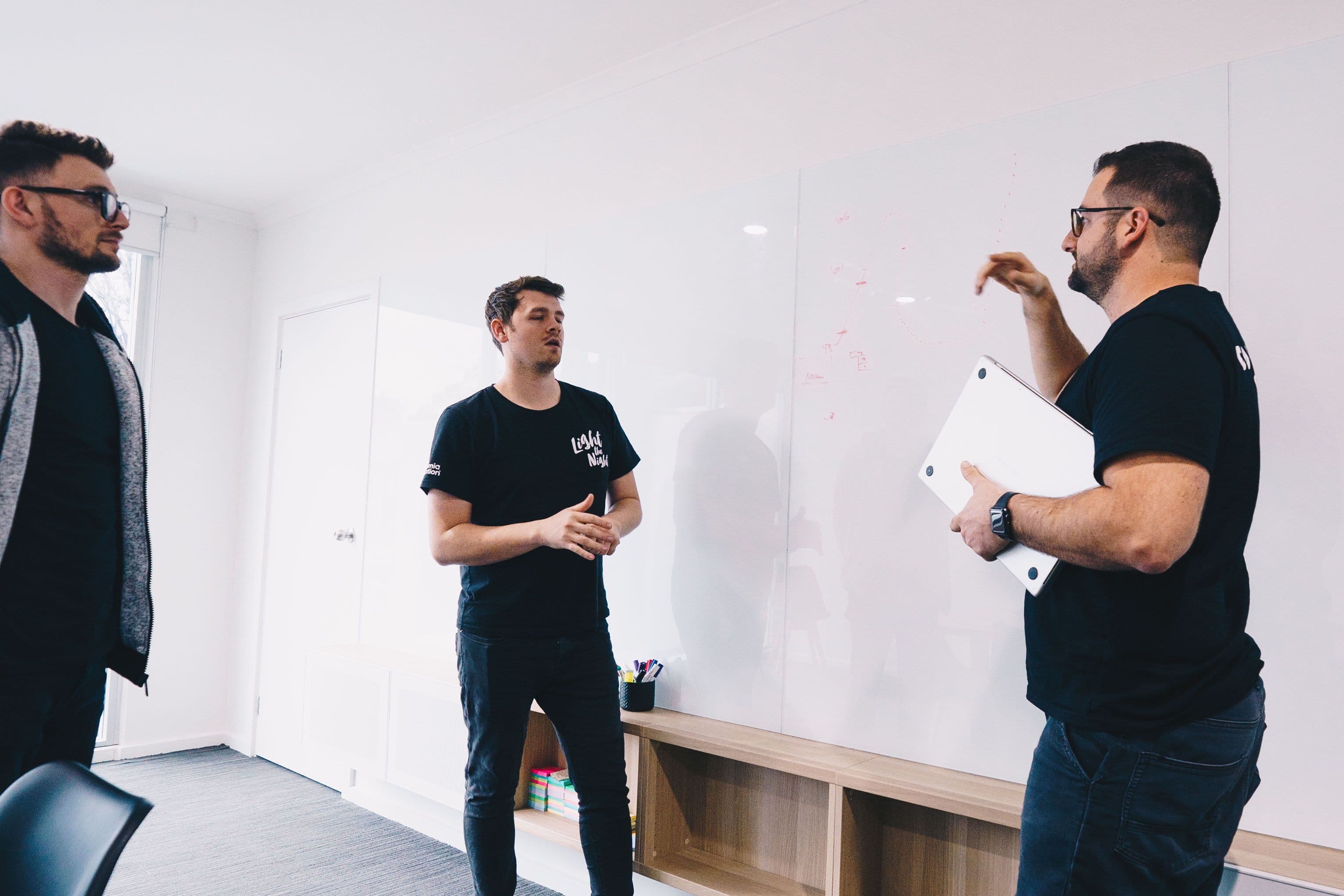 Three team members running a scoping discussion at a whiteboard, one holding a laptop